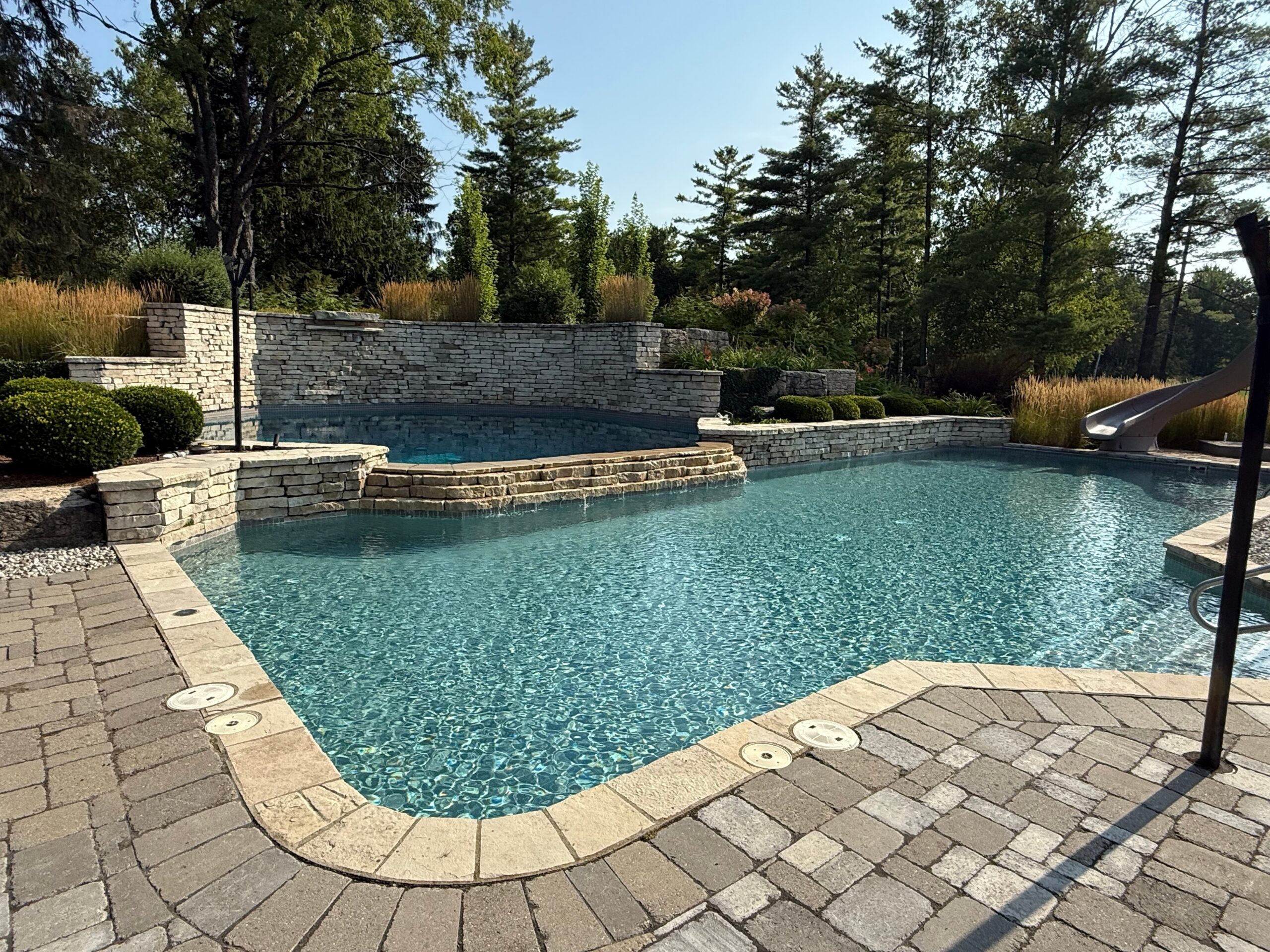 Backyard pool with stone walls and a wide deck, pool design inspiration